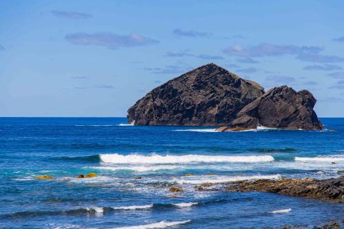 a large rock in the ocean with waves at Mosteiros Beach House in Ponta Delgada