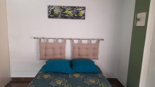 a bed with two blue pillows in a room at Bungalow charmant à Saint Paul avec terrasse et jardin privatif in Saint-Paul