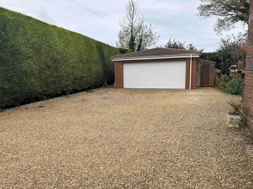 a driveway with a white garage next to a hedge at Entire guest suite with gated property in Broad Blunsdon