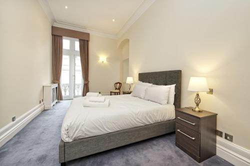 1 dormitorio con 1 cama blanca grande y mesita de noche en Historic Whitehall flat in SW1 by UnderTheDoormat en Londres