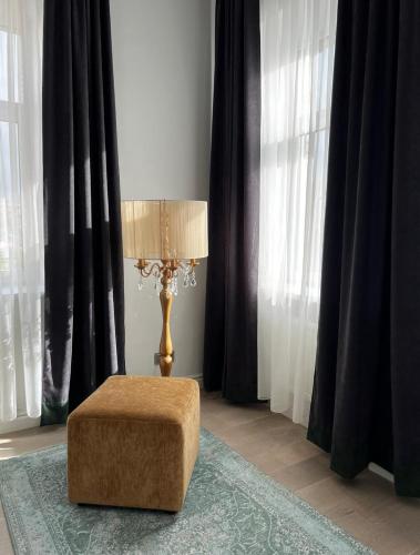 a lamp and a ottoman in a room with curtains at Raina apartment Gold in Jelgava