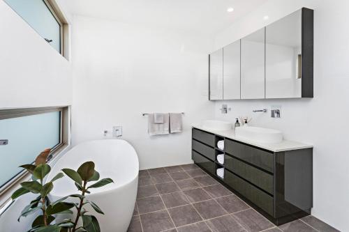 een badkamer met een bad, een wastafel en een spiegel bij Beachfront Bliss in Shellharbour
