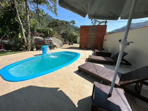 a swimming pool with an umbrella and some chairs at Sítio Morada do Pai: Piscina e Descanso in Canelinha