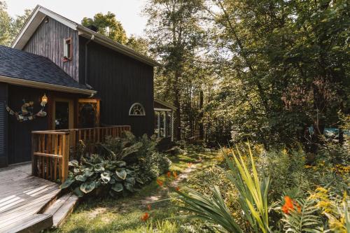 a black house with a deck and a garden at Auberge Yoga Salamandre in Lac-Brome