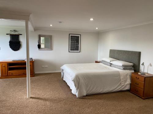 a bedroom with a large white bed and a dresser at Churchill Oasis by the sea in Tauranga