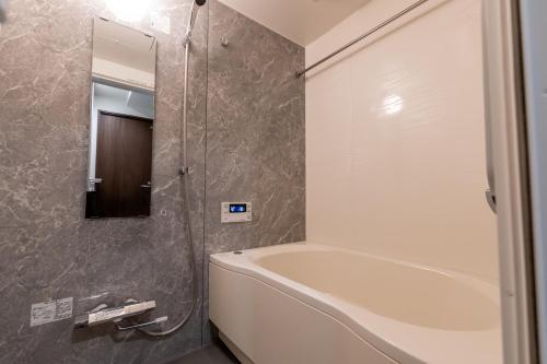 La salle de bains est pourvue d'une baignoire, d'une douche et d'un miroir. dans l'établissement Crest Otemae Stay - Self Check-In Only, à Osaka