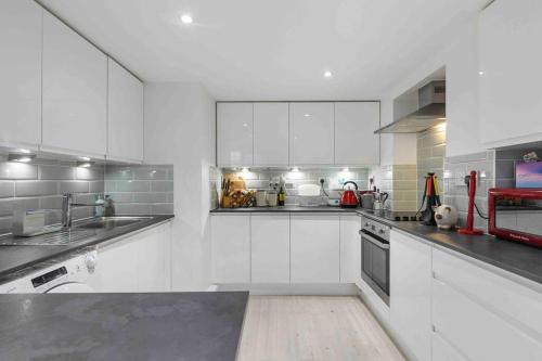 a large white kitchen with white cabinets and appliances at Little Venice Garden Apartment in London