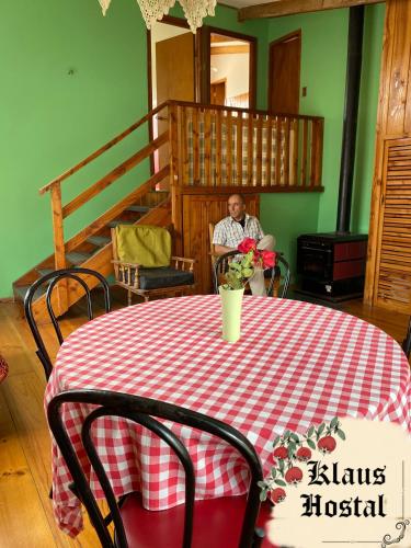 un hombre sentado en una mesa con un mantel rojo y blanco a cuadros en Hostal Klaus en Pucón