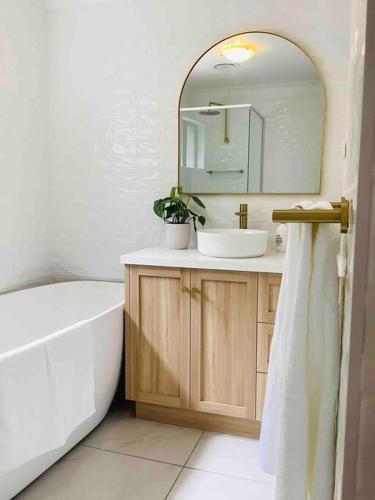 a bathroom with a sink and a tub and a mirror at Seabreeze Luxury Apartment Kiama in Kiama