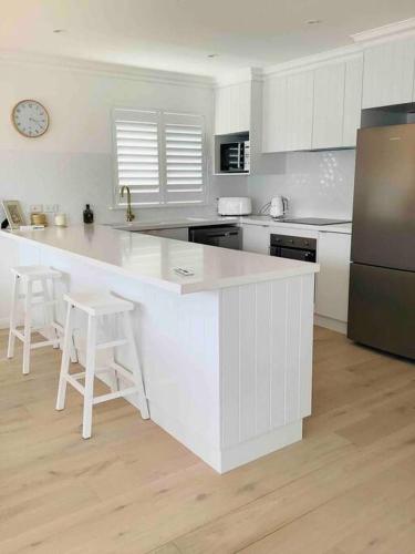 a white kitchen with a large white counter and stools at Seabreeze Luxury Apartment Kiama in Kiama