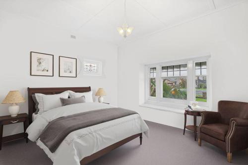 een witte slaapkamer met een bed en een stoel bij Glenelg Beach Bungalow in Glenelg