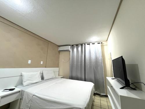 a bedroom with a white bed and a television at Flat number one temporadalitoranea in São Luís