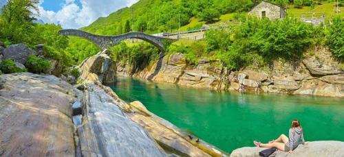 uma mulher sentada numa rocha perto de um rio com uma ponte em Le Palme em Monte Ceneri