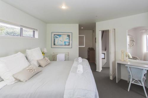 a white bedroom with a large bed and a sink at Chester Cottage Beachfront in Oakura