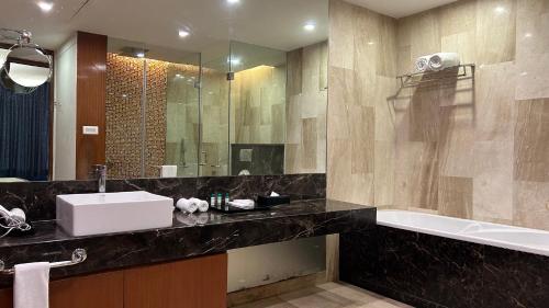 een badkamer met een wastafel, een bad en een spiegel bij The Conway in Meerut