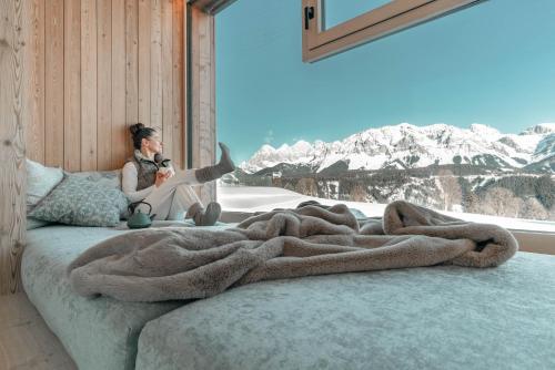 a woman sitting on a bed looking out a window at Apart & Suiten Hotel WEIDEN in Schladming