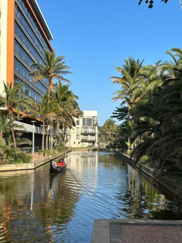 a boat in a canal with palm trees and buildings at DNA Dream Home in Durban