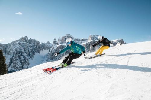 two people are skiing down a snow covered mountain at Pension Panorama in San Lorenzo di Sebato