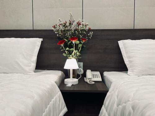 two beds with a table with a vase of flowers and a phone at Huy Hoàng Hotel Phan Thiet in Phan Thiet