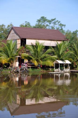 a building with palm trees in front of a body of water at Bungalow - Farmstay Hoa Rừng U Minh in Cà Mau