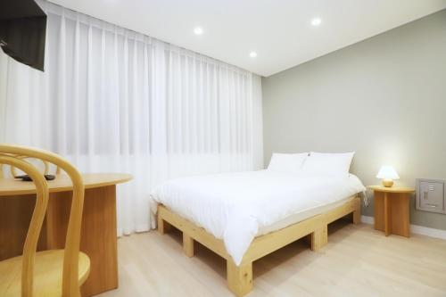 a white bedroom with a bed and a desk and a window at DADA house in Seoul