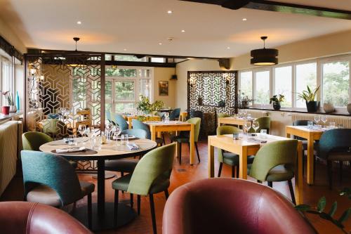 un restaurante con mesas, sillas y ventanas en Logis Hotel Le Relais De La Poste Restaurant Le Fil du Temps, en Thury-Harcourt