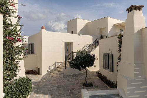 a white house with stairs and a tree in the courtyard at Proteas Hotel & Suites in Agios Prokopios