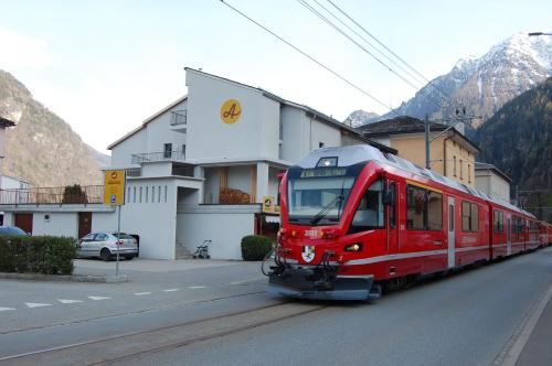 un treno rosso che viaggia lungo una strada con un edificio di B&B Alpina a Le Prese