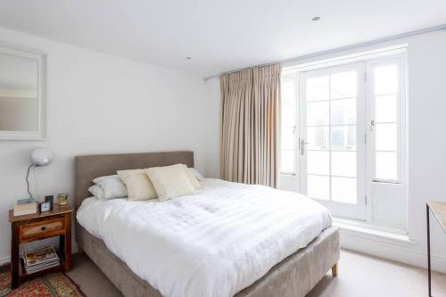 um quarto branco com uma cama e uma janela em Peaceful and Quiet 1BR Cottage in Camberwell em Londres