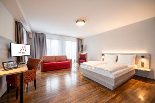ケルンにあるエデン ホテル フルー アム ドムのベッドと赤いソファが備わるホテルルームです。