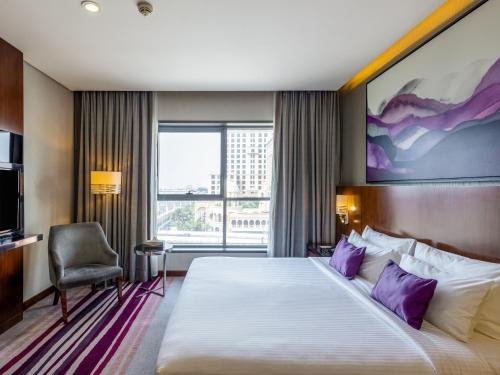 Flora Al Barsha Hotel At The Mall في دبي: غرفة في الفندق مع سرير كبير مع وسائد أرجوانية