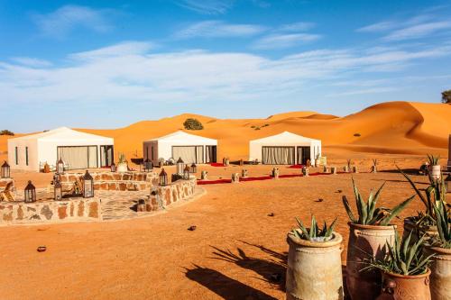 a group of tents in the desert with sand dunes at Merzouga luxury desert camps in Merzouga