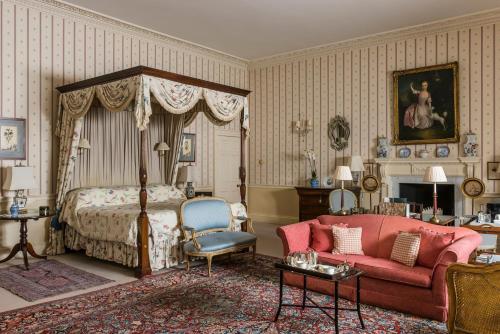 a bedroom with a canopy bed and a red couch at Hartwell House & Spa in Aylesbury