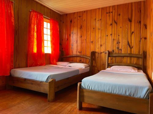 two beds in a wooden room with red curtains at Saint Joseph Inn in Sagada