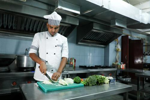 a chef cutting up vegetables on a counter in a kitchen at Hotel Sharda Residency in Patna