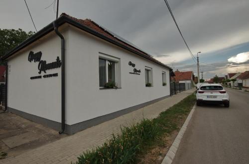 a small white building with a car parked next to it at Happy Moments Apartman in Gyula
