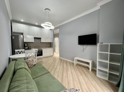 Una sala de estar con un sofá verde y una cocina. en Приятные апартаменты в элитном комплексе, en Almaty