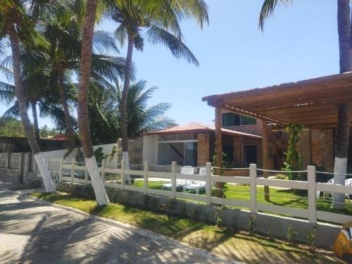 a white fence in front of a house with palm trees at Pousada Fenícia in Japaratinga