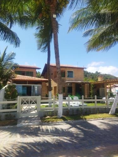 a house with a white fence and palm trees at Pousada Fenícia in Japaratinga