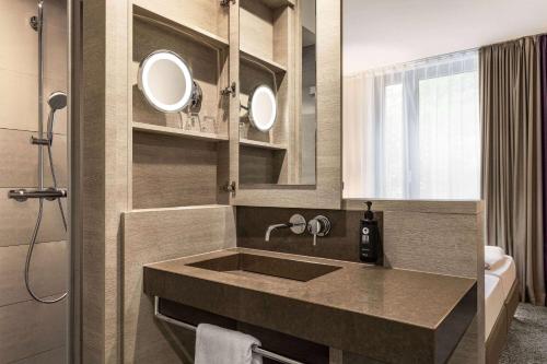 a bathroom with a sink and two mirrors at Vienna House Easy by Wyndham Osnabrück City & Apartments in Osnabrück