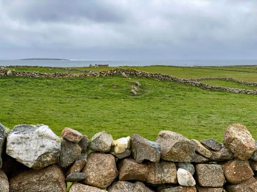 a stone wall in a field with a horse in the distance at Cottage 383 - Claddaghduff in Claddaghduff
