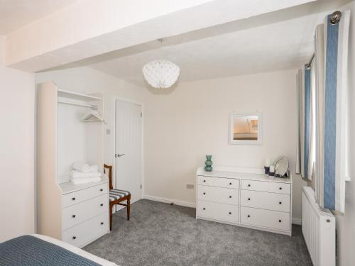 a white bedroom with a bed and a dresser at Llwyn Eithin in Holyhead