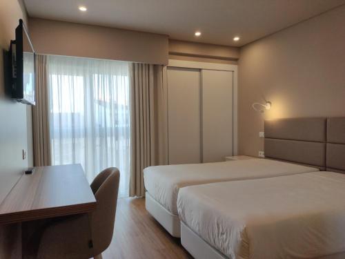 a hotel room with two beds and a desk and a window at Hotel Cristal Caldas in Caldas da Rainha
