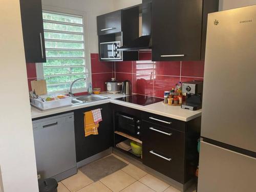 eine kleine Küche mit schwarzen Schränken und roten Wänden in der Unterkunft Le Ti Mimosa - Lagon in Saint-Leu