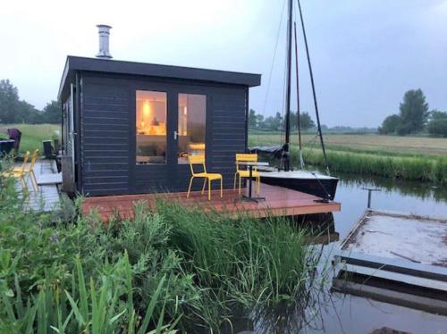 a tiny house on a dock next to a boat at Mooie woonboot op eiland, kachel, natuur, sloep! in Grou