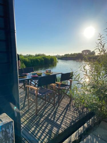 a table and chairs on a deck next to a river at Mooie woonboot op eiland, kachel, natuur, sloep! in Grou