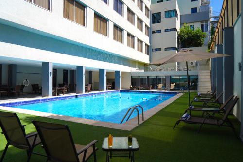 einem Pool mit Stühlen und einem Sonnenschirm neben einem Gebäude in der Unterkunft MENA Tyche Hotel Amman in Amman