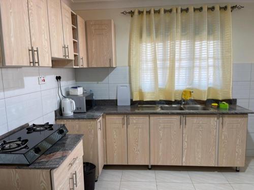 cocina con armarios de madera, fregadero y ventana en Munyonyo Apartment, en Kampala