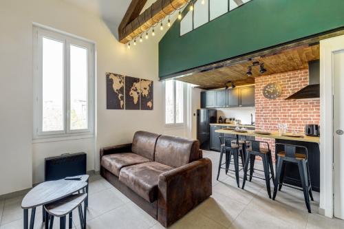 a living room with a leather couch and a kitchen at L'Industrie-Loft-T2-Clim-Parking à proximité in Pierre-Bénite