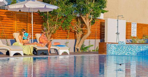 two women sitting in chairs next to a swimming pool at Sunny Days Hotel in Ixia